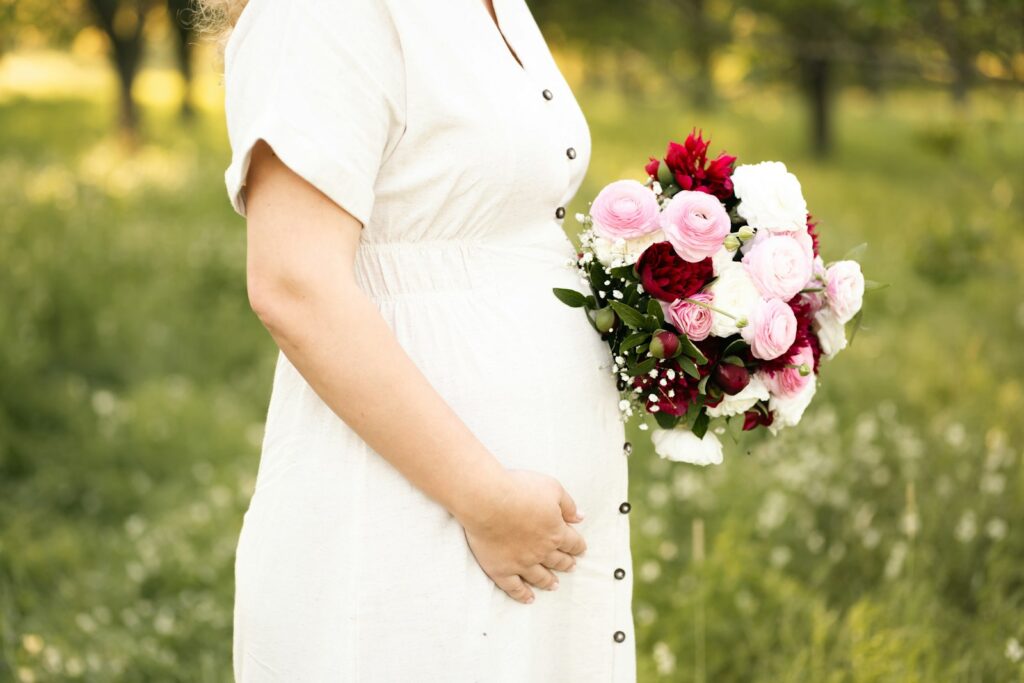 Braut im Umstandsbrautkleid mit lockerem Brautstrauß im Garten