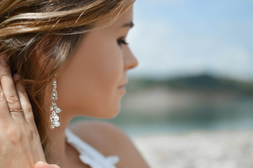 Brautschmuck mit Perlenohrringen und feiner Kette auf einem Brautkleid aus Spitze