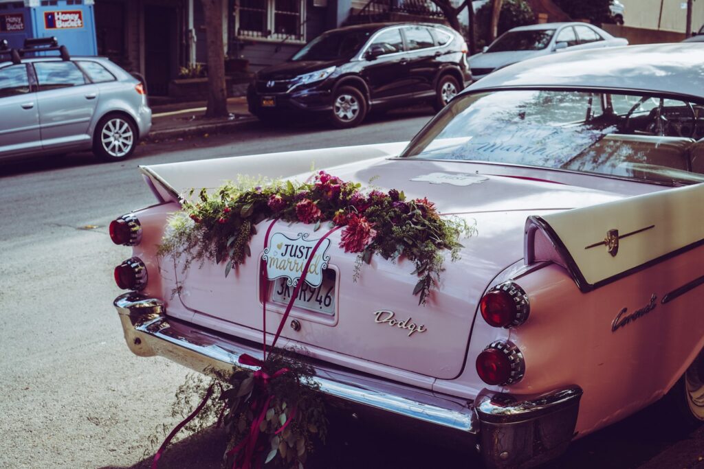 Geschmücktes Hochzeitsauto, ein heller Oldtimer mit Blumenschmuck vor einer Kirche