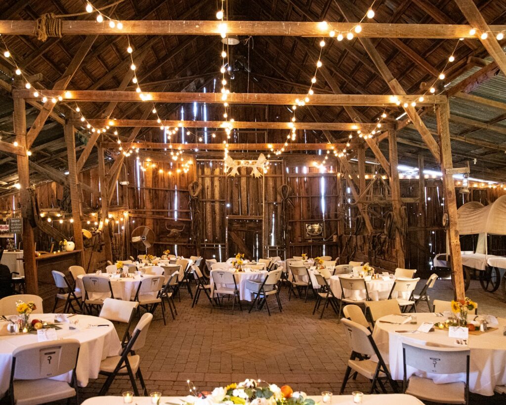 Hochzeit Scheune: festlich gedeckte lange Tafeln unter Holzbalken mit Lichterketten