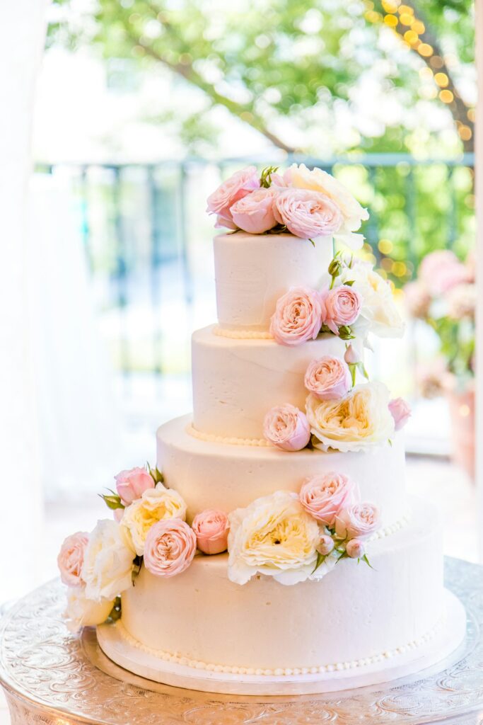 Hochzeitstorte mit drei Etagen, weißer Buttercreme und frischen Blüten auf einem Holztisch