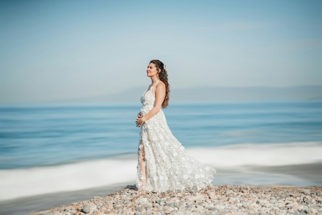 Schwangere Braut im Umstandsbrautkleid mit Empire-Taille hält ihre Hände auf dem Babybauch