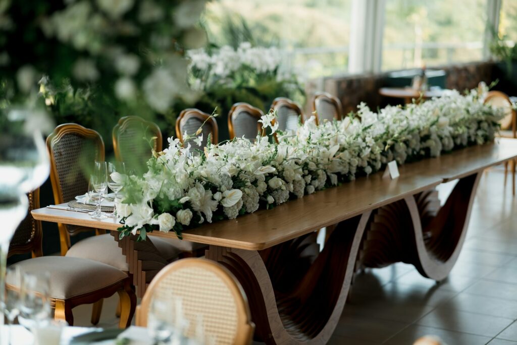 Tischdeko Hochzeit an einer langen Tafel mit saisonalen Blumen, Leinenläufer und Stabkerzen